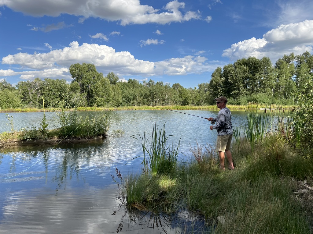Angler casting on a private pond under blue Montana sky