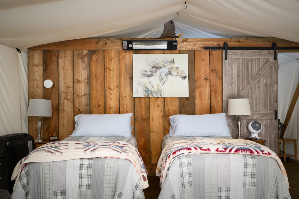 Two neatly made twin beds face a wood-plank wall with a running-horse painting and a wide barn-style sliding door.