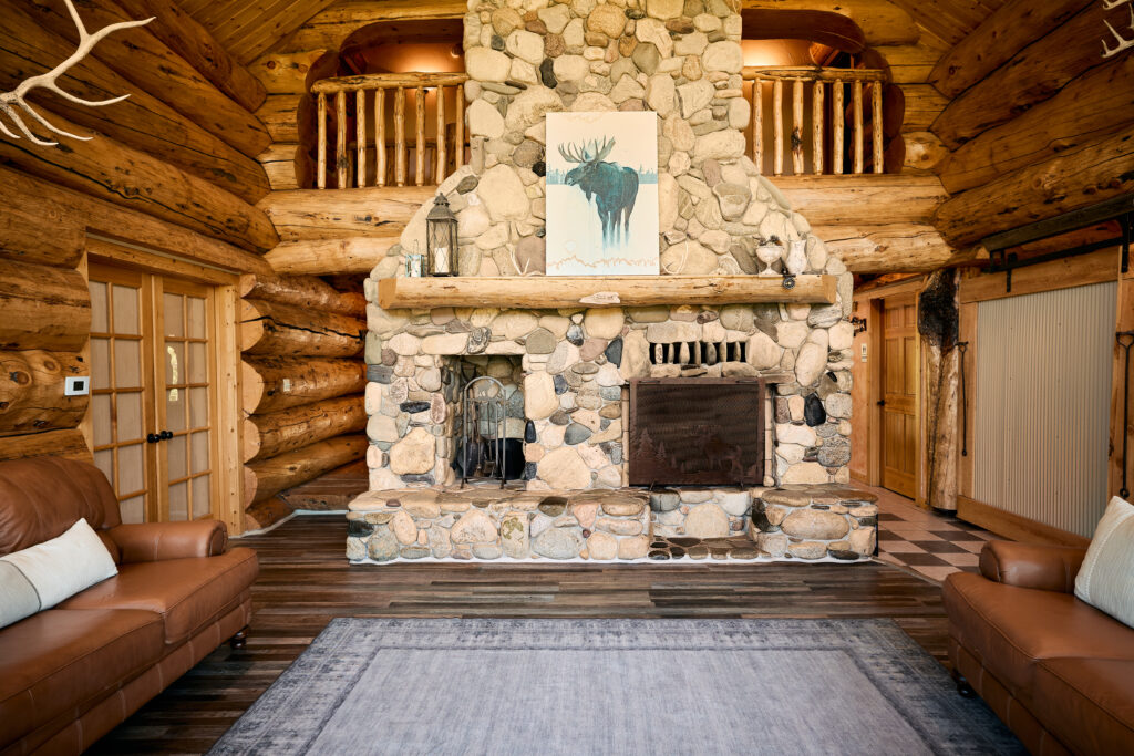 A stone fireplace in the great room with a moose painting above the mantel, flanked by leather sofas