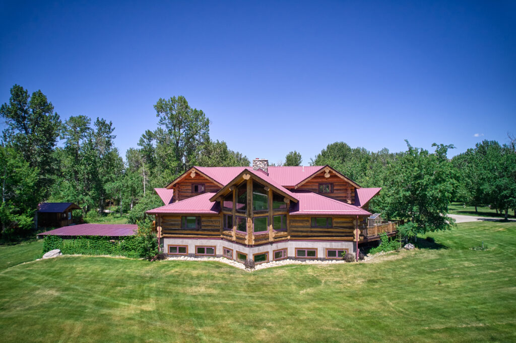 A wide ground-level view of the log lodge's roofline and grounds, framed by tall trees