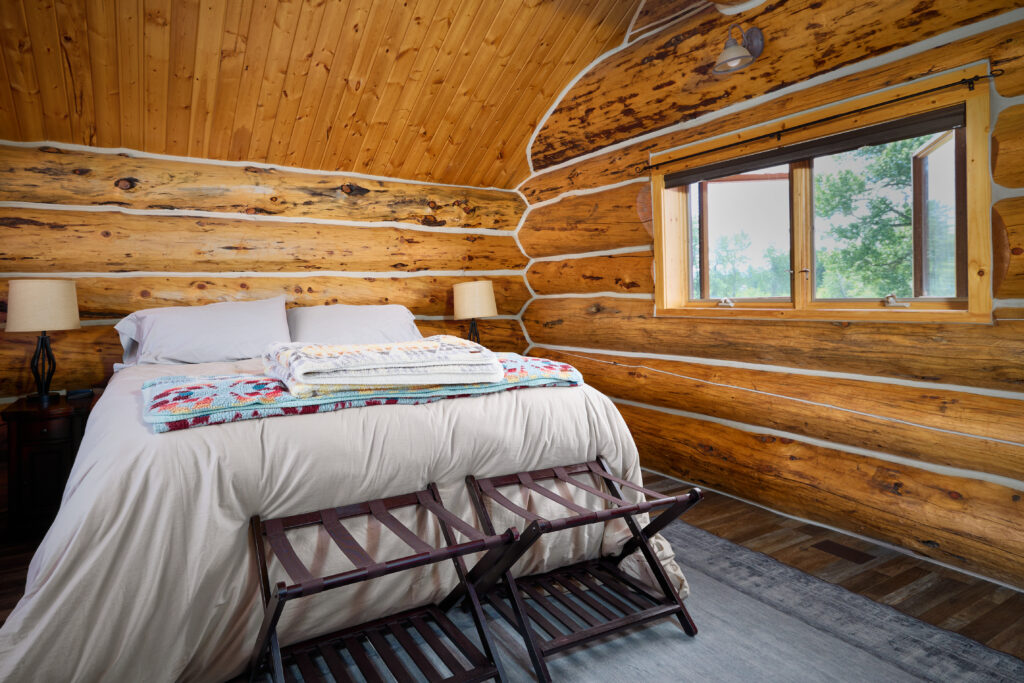 A neatly made bed with folded quilts sits beneath log walls in a Flagship Lodge bedroom