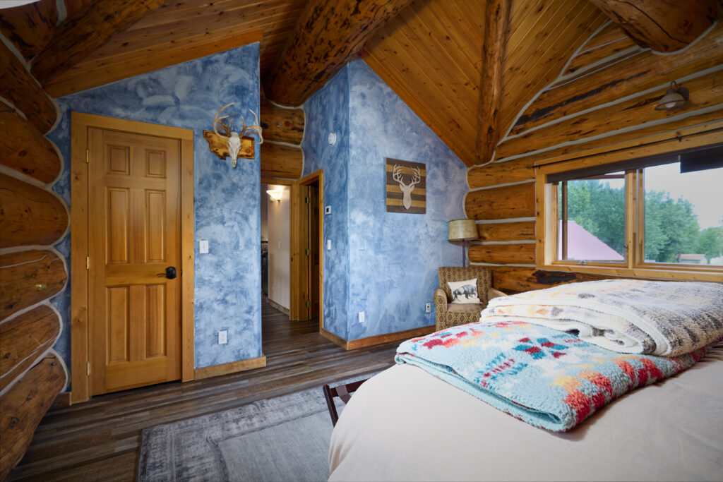 A bedroom with hand-painted blue walls, mounted antlers, and a doorway opening to an adjoining room