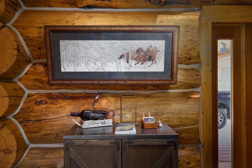 A rustic entry console below a framed painting of horseback riders, set against exposed log walls