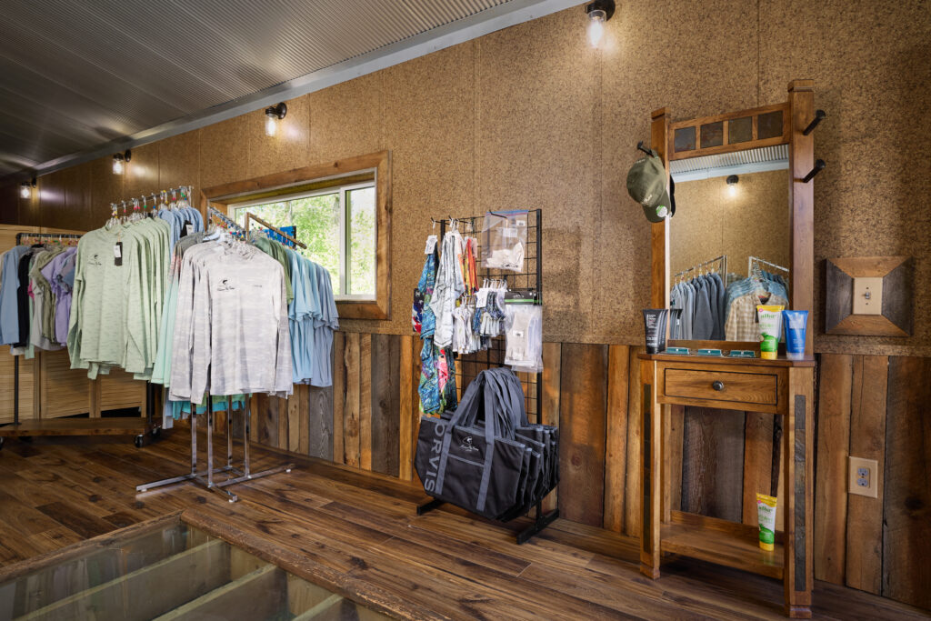 Pro shop apparel racks and an Orvis duffel bag beside a wooden vanity with a mirror and grooming products