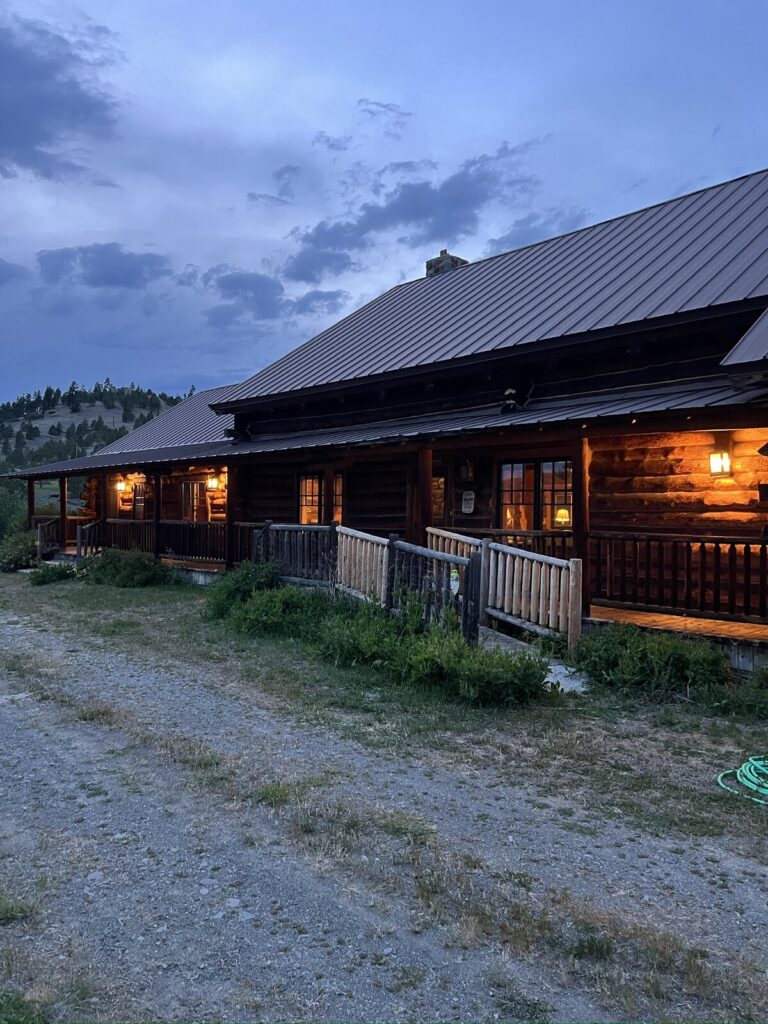 Spring Creek Lodge log exterior at dusk with warm-lit windows and a wraparound porch