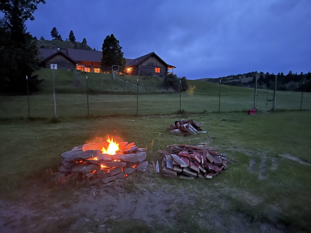 A roaring fire pit at dusk with the lit lodge in the background