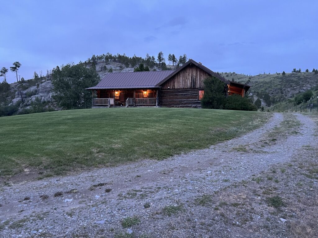 Spring Creek Lodge on a grassy hillside with a curving drive at dusk