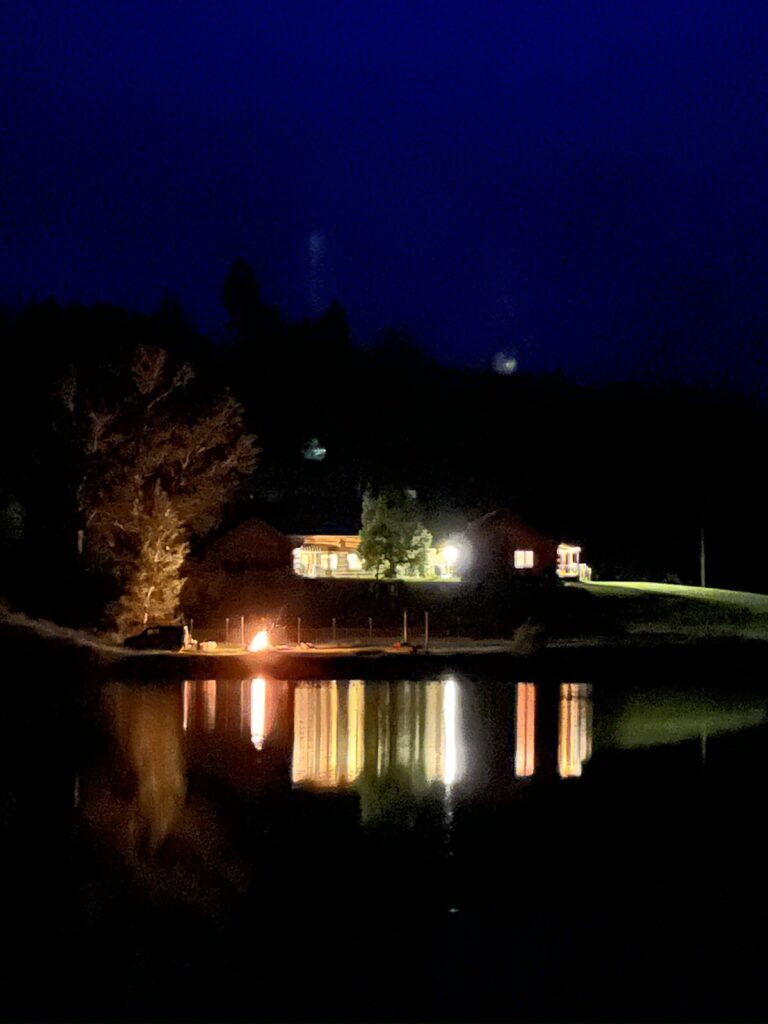 Spring Creek Lodge lit at night and reflected across the pond beside a streamside fire